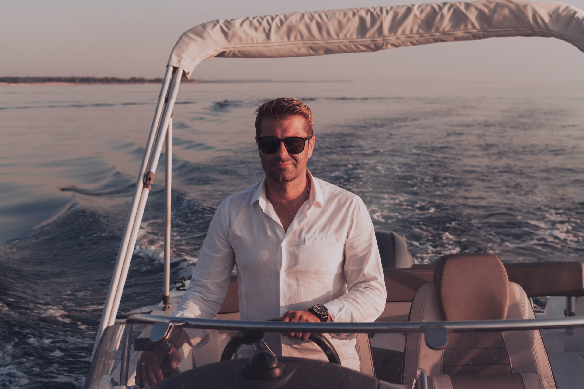 Sustainable Luxury Fashion: How to Build an Eco-Conscious Designer Wardrobe A determined senior businessman in casual clothes and sunglasses enjoys his vacation driving a luxury boat at sunset.